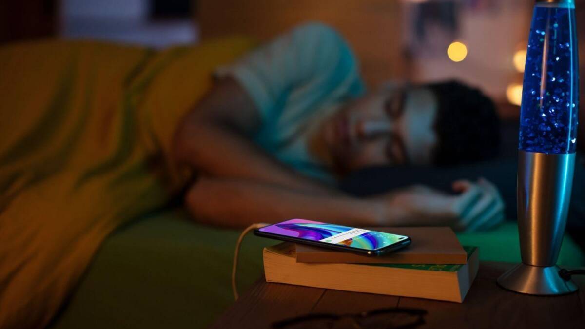 Женщина спит на кровати рядом с OPPO Reno4 Lite и лампой