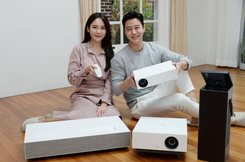 Пара сидит на полу с белым проектором LG 4K