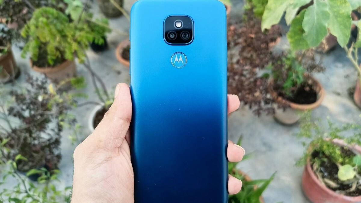 Мобильный телефон Motorola Moto E7 в руке на фоне горшков с растениями