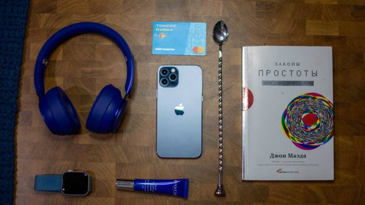 На деревянной поверхности расположены наушники, iPhone, часы и книга