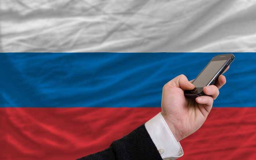 Человек держит смартфон на фоне российского флага