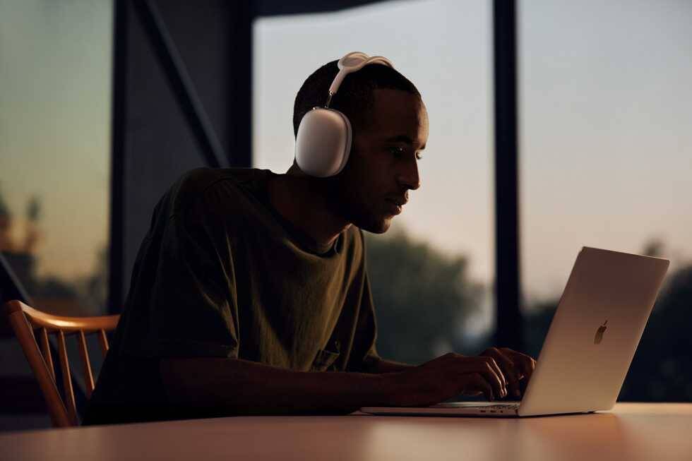 Человек с наушниками AirPods Max за ноутбуком в сумерках