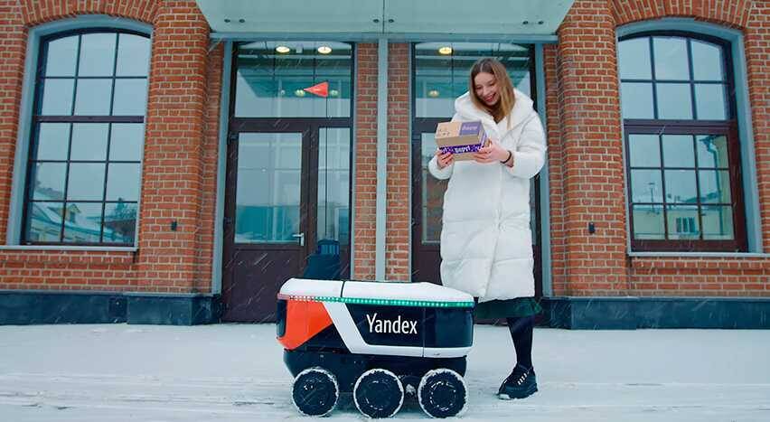 Девушка с посылками рядом с роботом Яндекс Ровер на улице