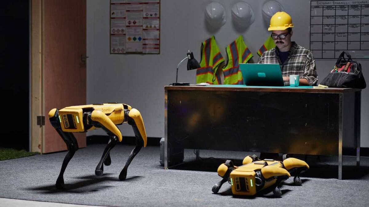 Роботы Boston Dynamics в офисной среде и человек в каске с ноутбуком