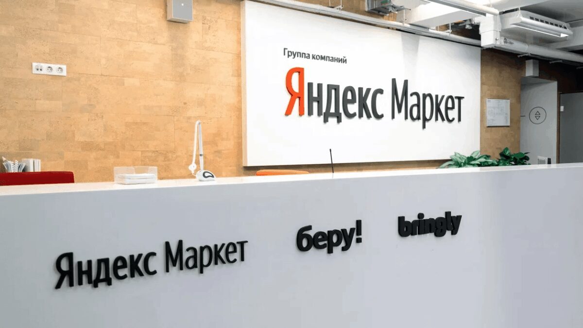 Белая стойка регистрации в офисе Яндекс.Маркет с логотипом и растением в боксе