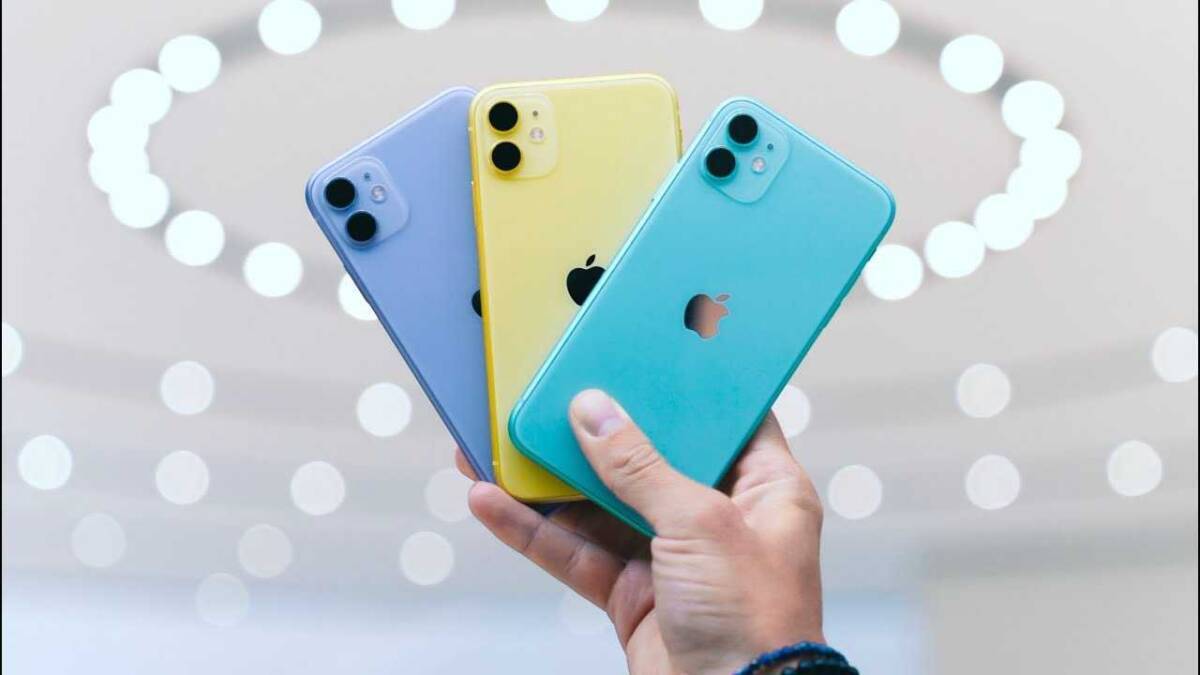 Цветные смартфоны iPhone 11 в руке на фоне светового оформления