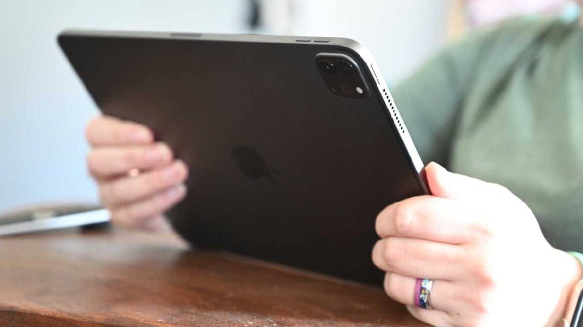 iPhone и iPad на руках человека, смартфон и планшет Apple на деревянной поверхности