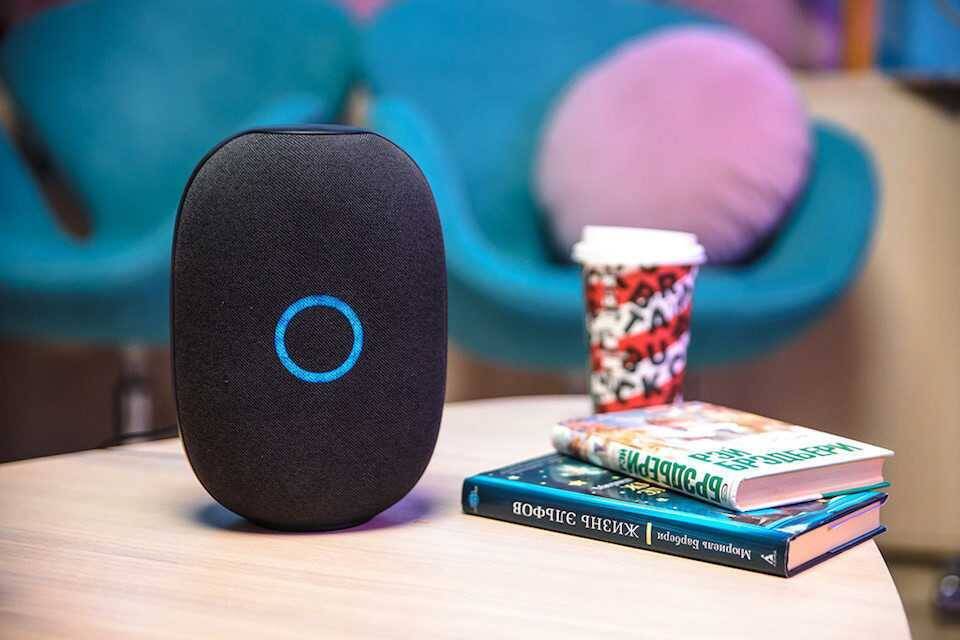 Умная колонка TP-Link на столе, синее кольцо индикатора, рядом книги и кофе