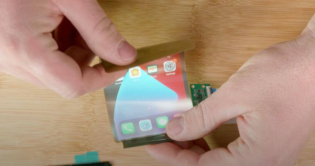 Кто-то сейчас делает складной iPhone, но не Apple 5 Человек держит складной экран iPhone с подсветкой