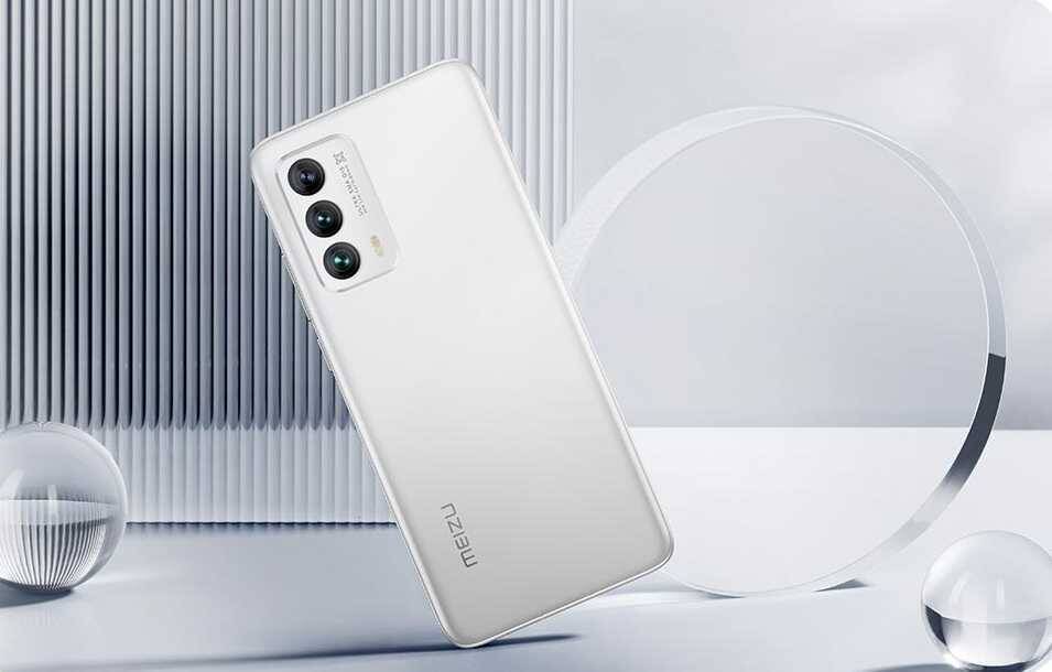 Белый смартфон Meizu 18 с тройной камерой в вертикальной ориентации на фоне абстрактного серого интерьера