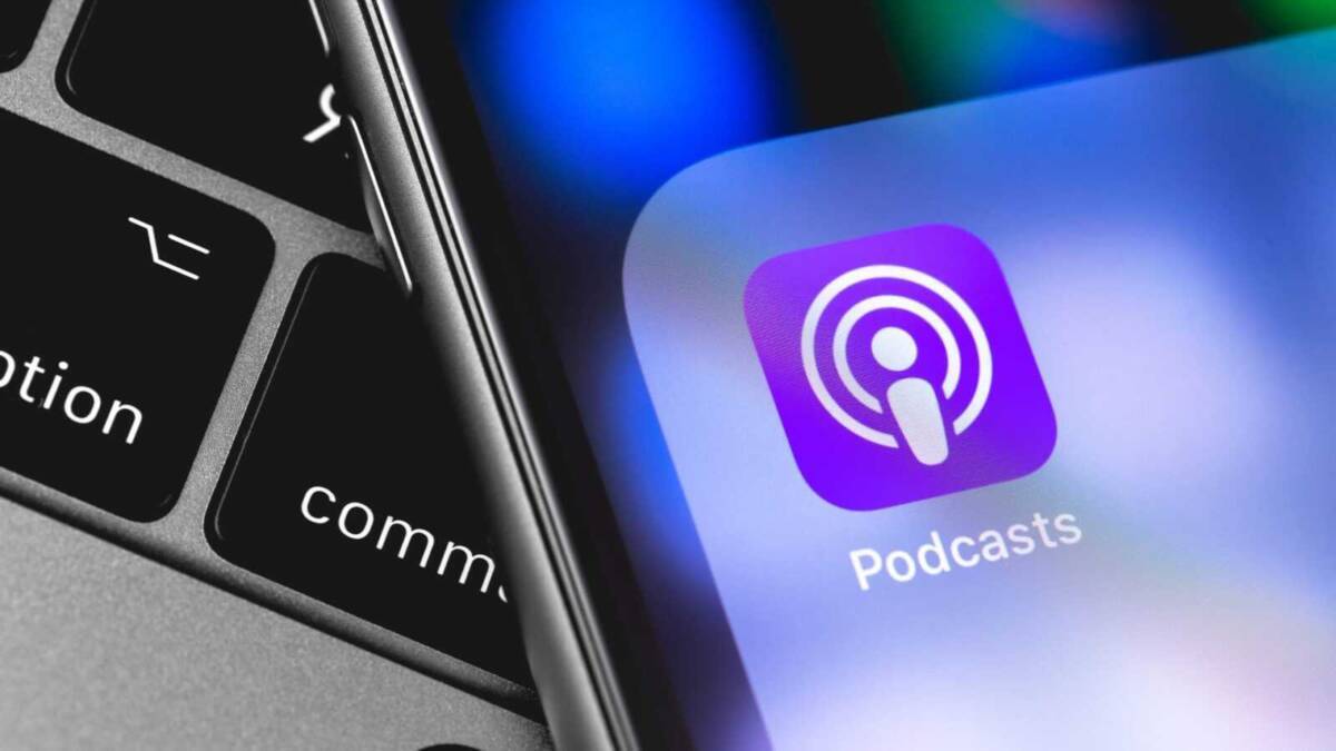 Экран iPhone с иконкой приложения «Подкасты» на фоне клавиатуры ноутбука