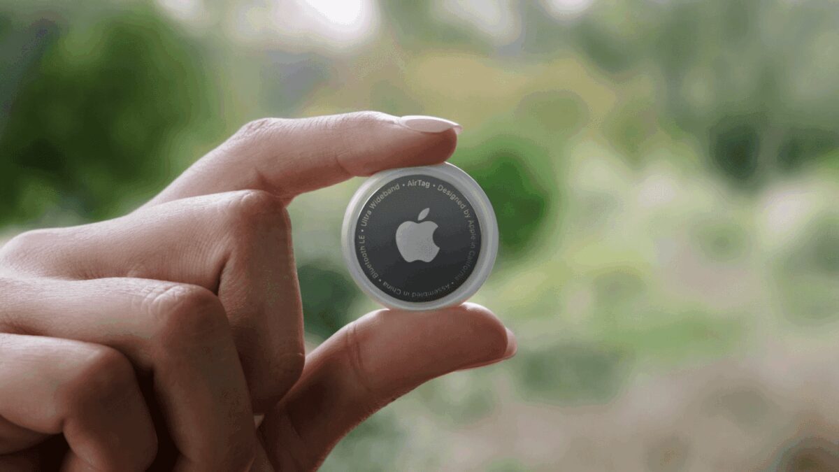 Рука держит круглый чип Apple AirTag на фоне природы