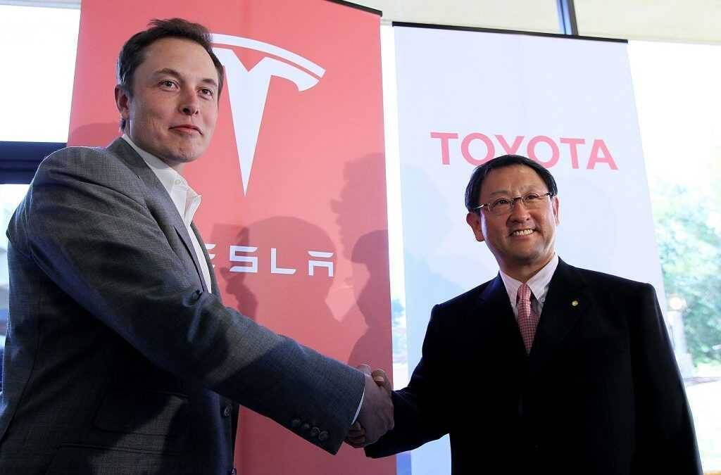 Подписание соглашения Tesla и Toyota: двое мужчин обмениваются рукопожатием на фоне логотипов компаний