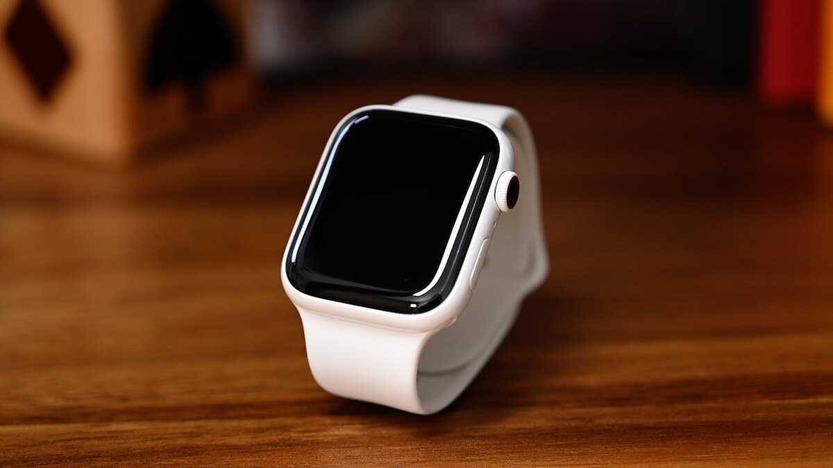 Умные часы Apple Watch с черным дисплеем и белым ремешком на деревянном столе