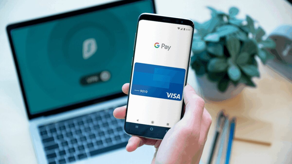 Смартфон с новым интерфейсом Google Pay и привязанной Visa картой перед ноутбуком