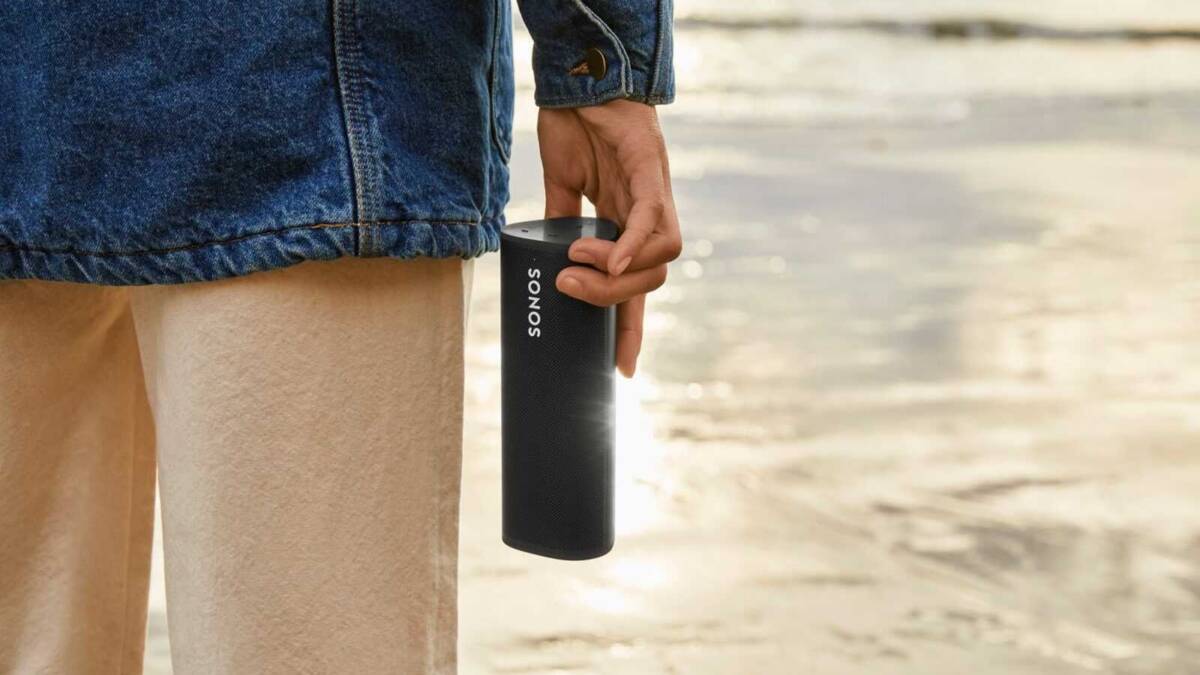 Человек держит портативную колонку Sonos Roam на пляже