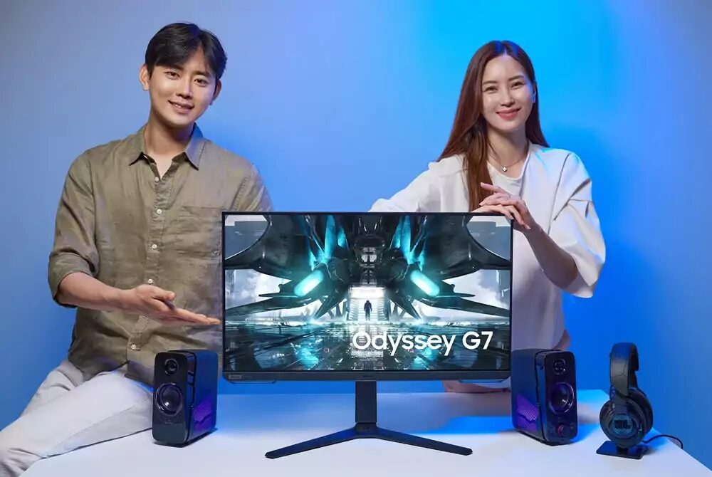 Два человека с монитором Odyssey G7 и акустическими системами на столе