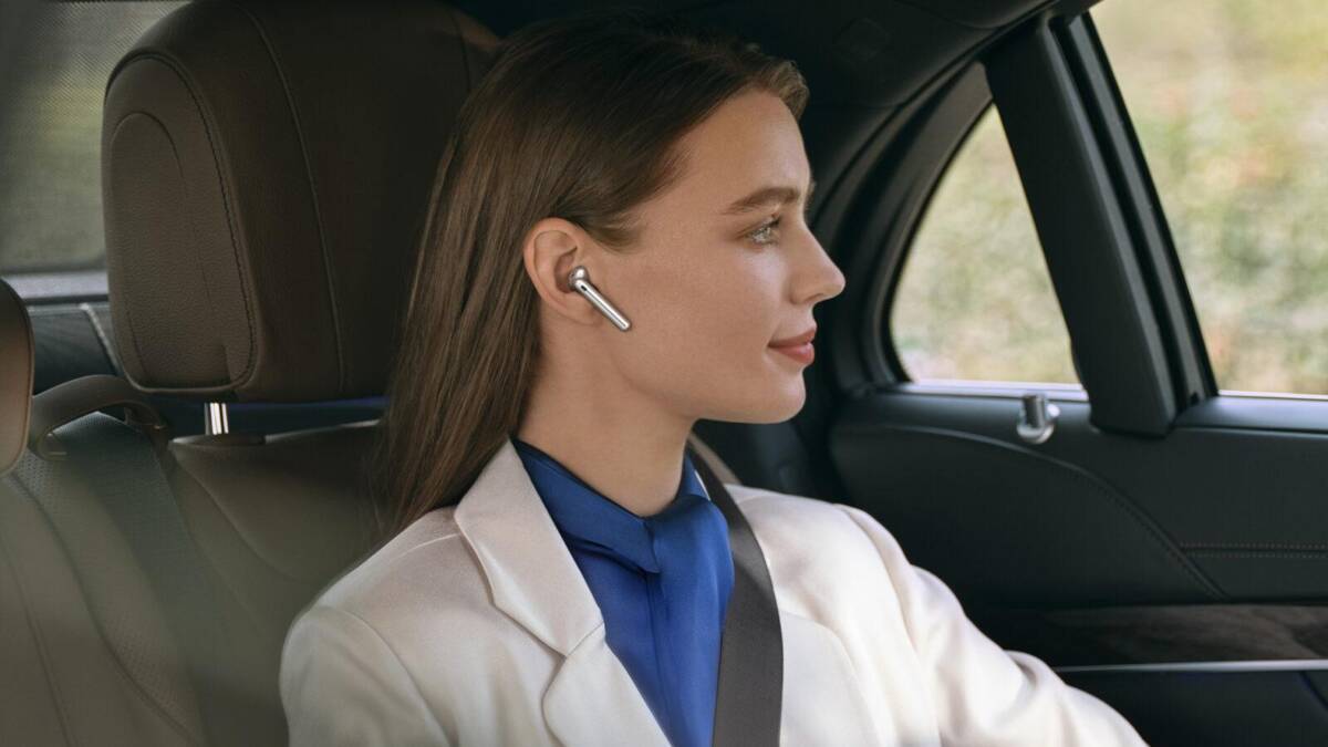 Блондинка в белом костюме и наушниках Huawei FreeBuds 4 сидит в машине