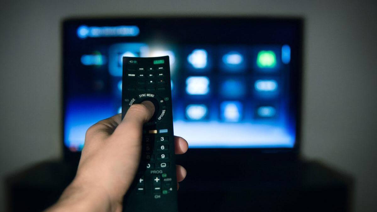 Девушка держит пульт дистанционного управления против телевизора с интерфейсом, крупный план