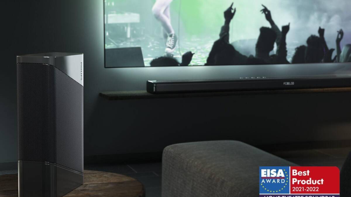 Домашняя музыкальная система Philips Fidelio B97 на деревянном столе со звуковой панелью в фоновом изображении