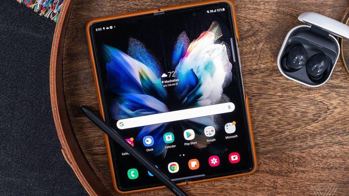 Складной смартфон Samsung Galaxy Z Fold на деревянном столе с пером и наушниками в чехле