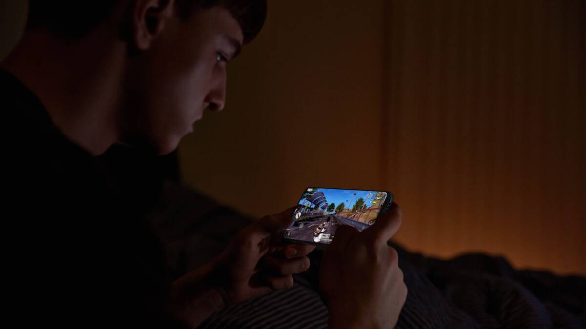 Человек играет в мобильную игру на смартфоне OPPO Reno6 в темной комнате