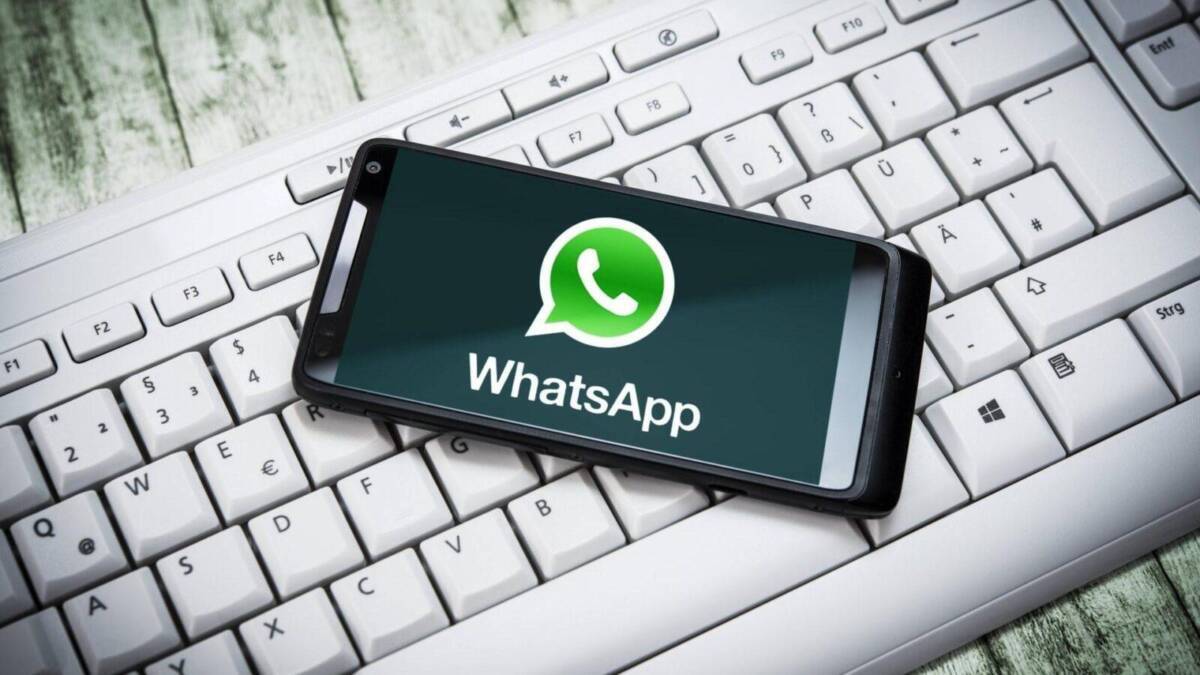 Смартфон с приложением WhatsApp на экране, логотип WhatsApp на фоне компьютерной клавиатуры