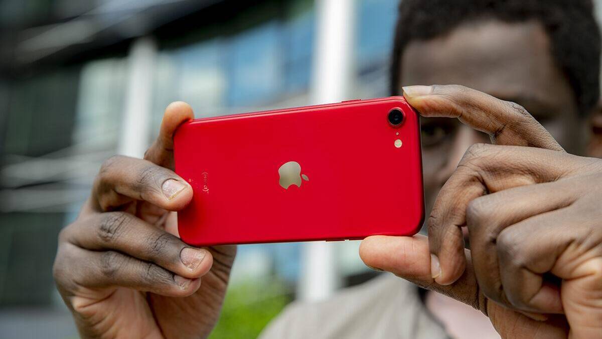 Человек фотографирует красный iPhone SE 3 с задней стороны