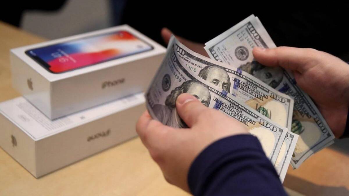 Человек держит наличные доллары перед коробкой iPhone