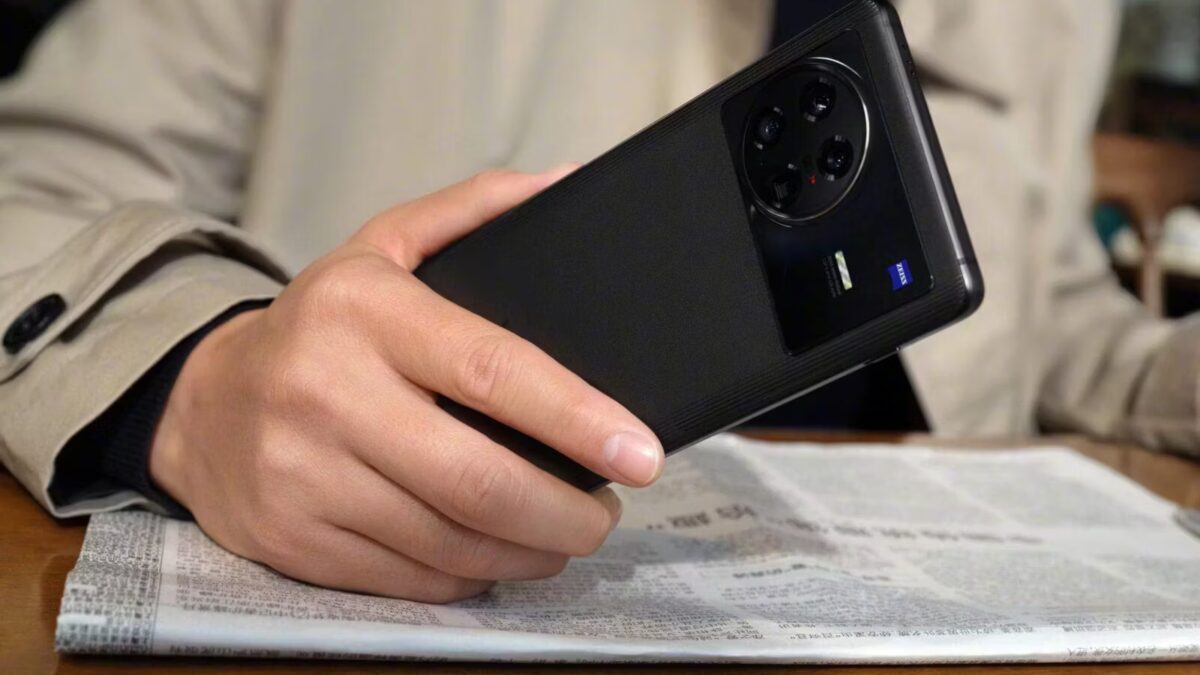 Рука держит смартфон Vivo X Note на столе, черный вариант, крупный план на фоне газеты