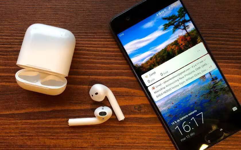 Беспроводные наушники AirPods с зарядным кейсом и смартфон на деревянной поверхности