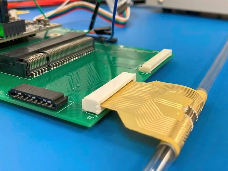 a green circuit board attached to a flexible golden chip wrapped around a thin tube.jpg