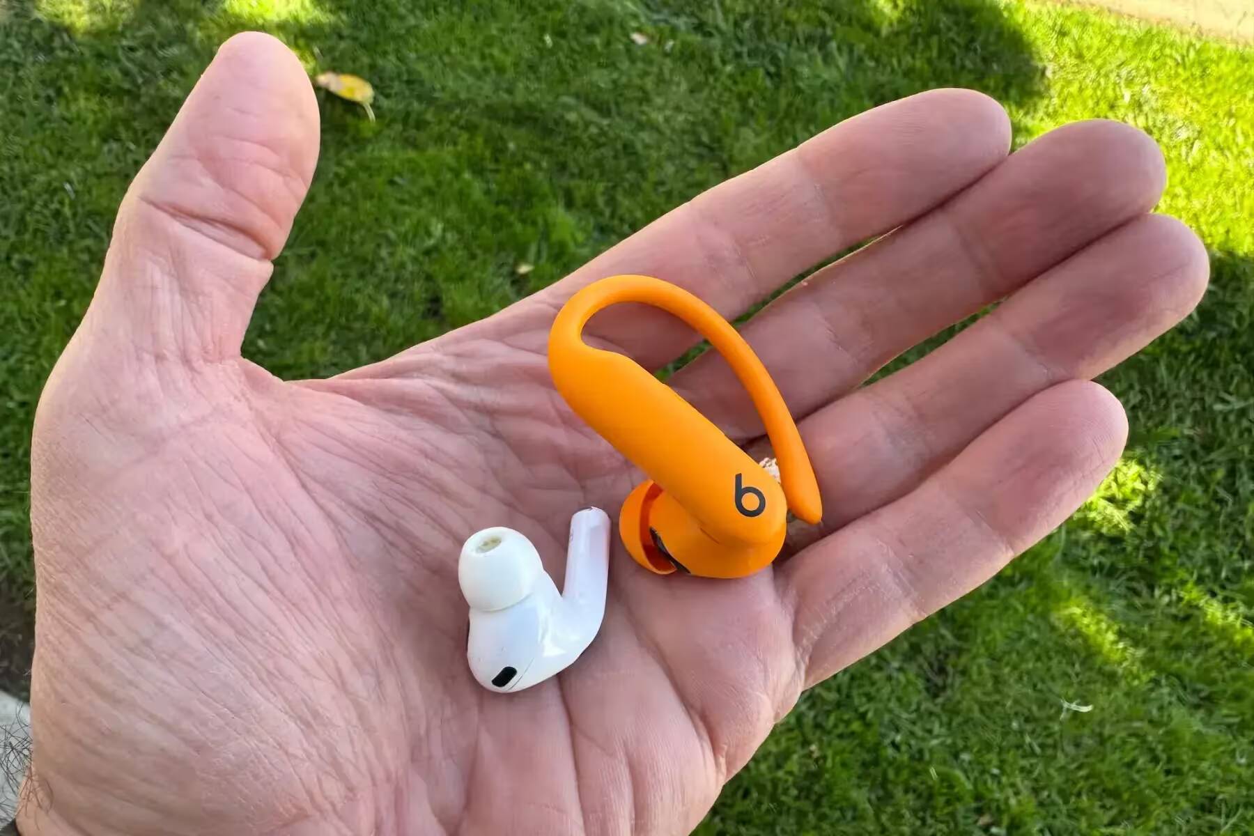 Вид на два беспроводных наушника Apple AirPods Pro 2 и Beats Powerbeats Pro 2 в руке на фоне травы