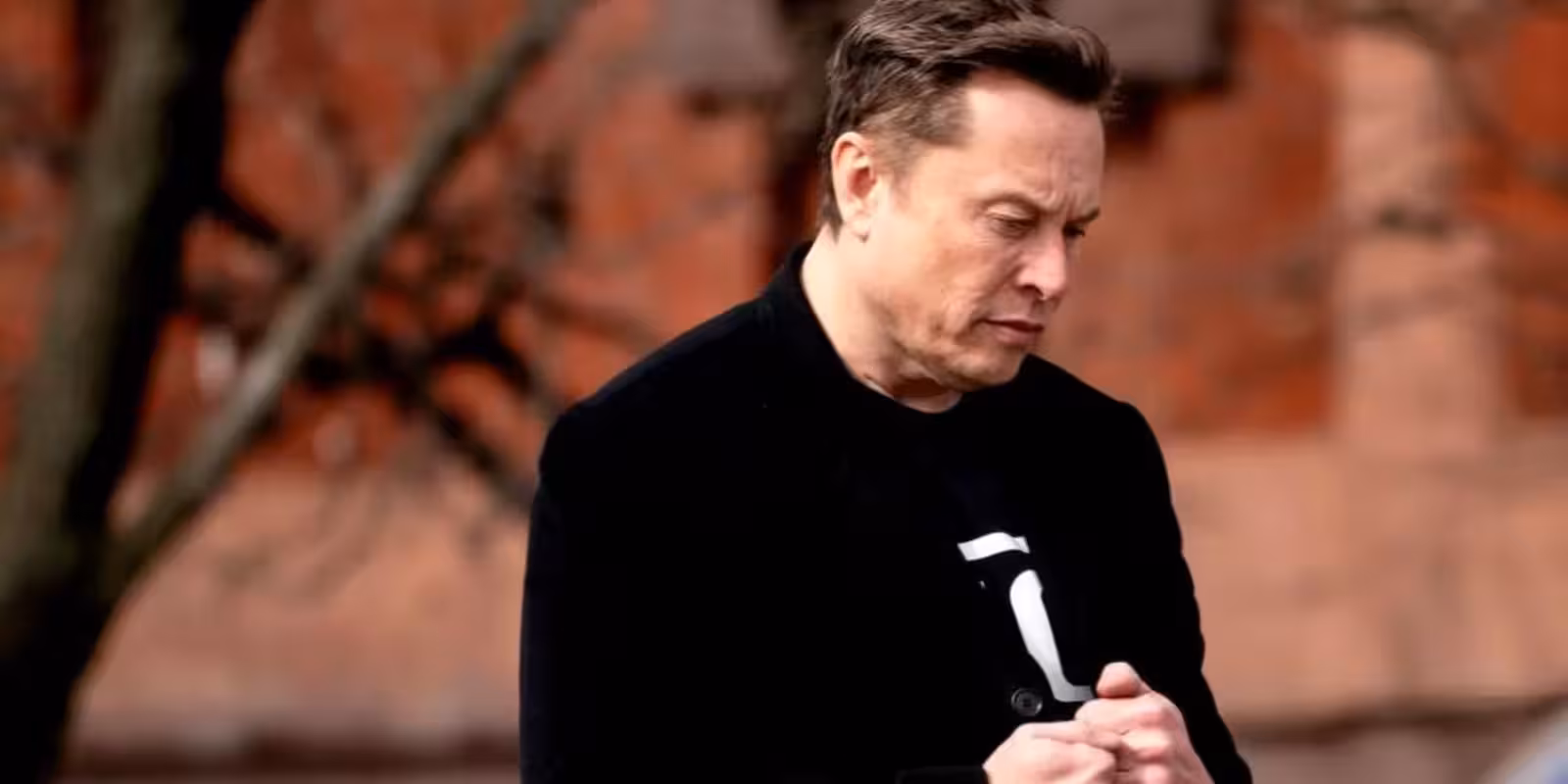 Мужчина в черной куртке в осеннем парке, задумчивый взгляд на фоне городской улицы