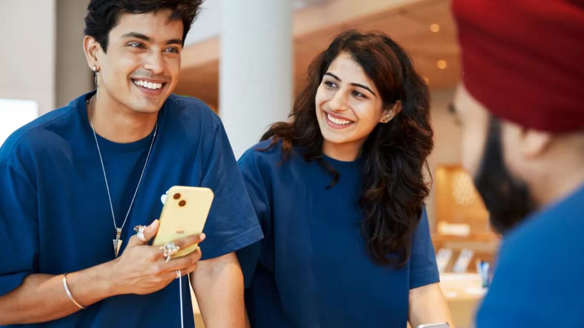 Две покупательницы общаются с консультантом в магазине электроники, на баннере iPhone и ИИ для продаж