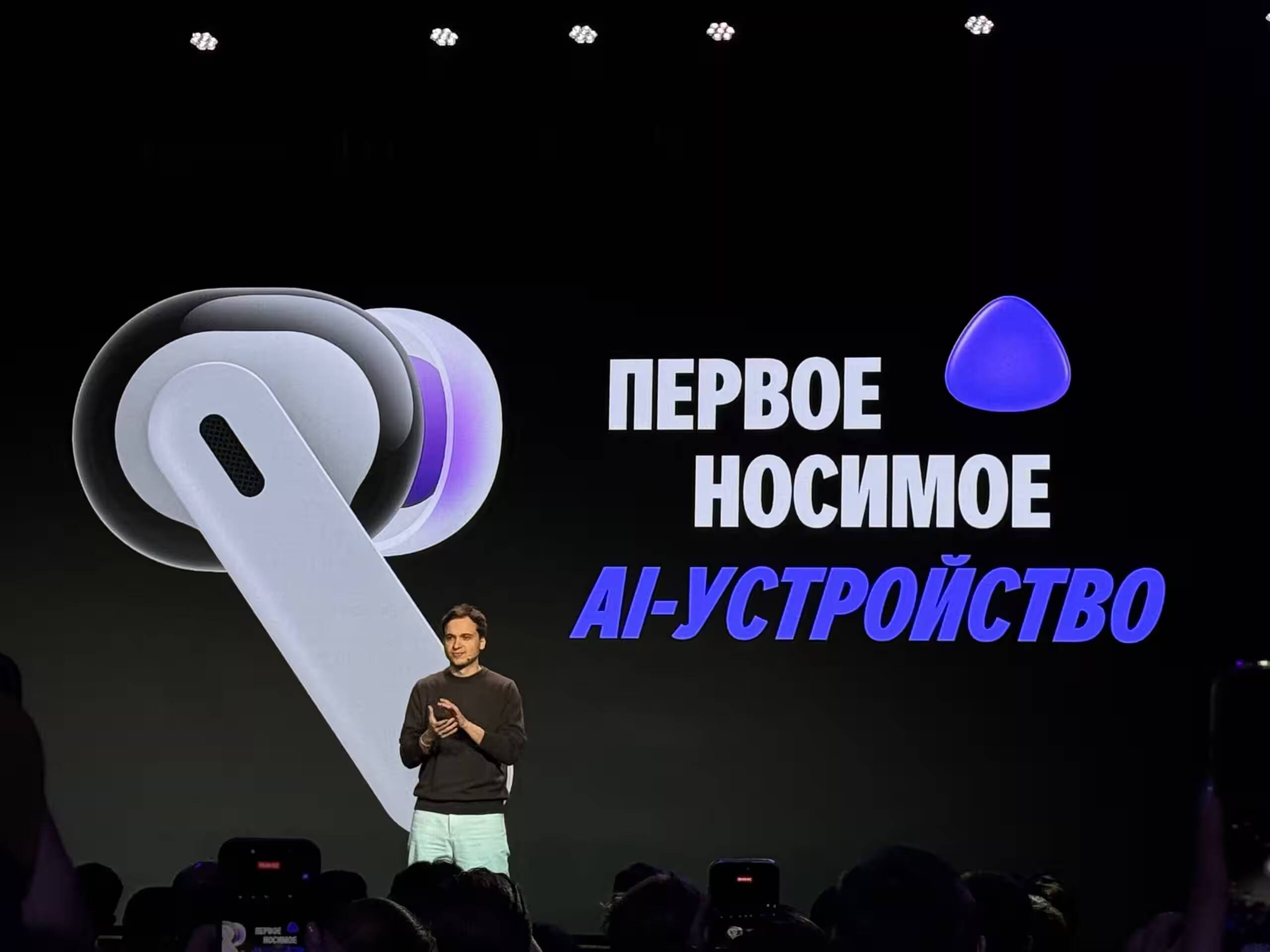 Яндекс анонсировал новую категорию носимых ИИ-устройств с Алисой AI 1 Презентация беспроводных наушников с логотипом Яндекса с человеком на сцене