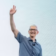 Человек в серой рубашке улыбается и машет рукой
