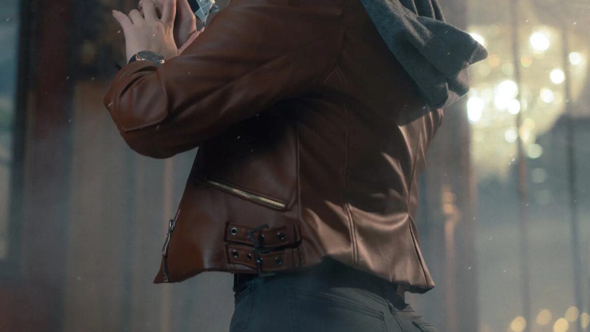 Женщина с короткими светлыми волнистыми волосами в коричневой куртке с пушистым капюшоном и джинсами в позе с пистолетом из сериала Resident Evil Requiem