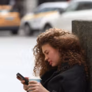 Женщина с кудрявыми волосами использует телефон, кофе в руке