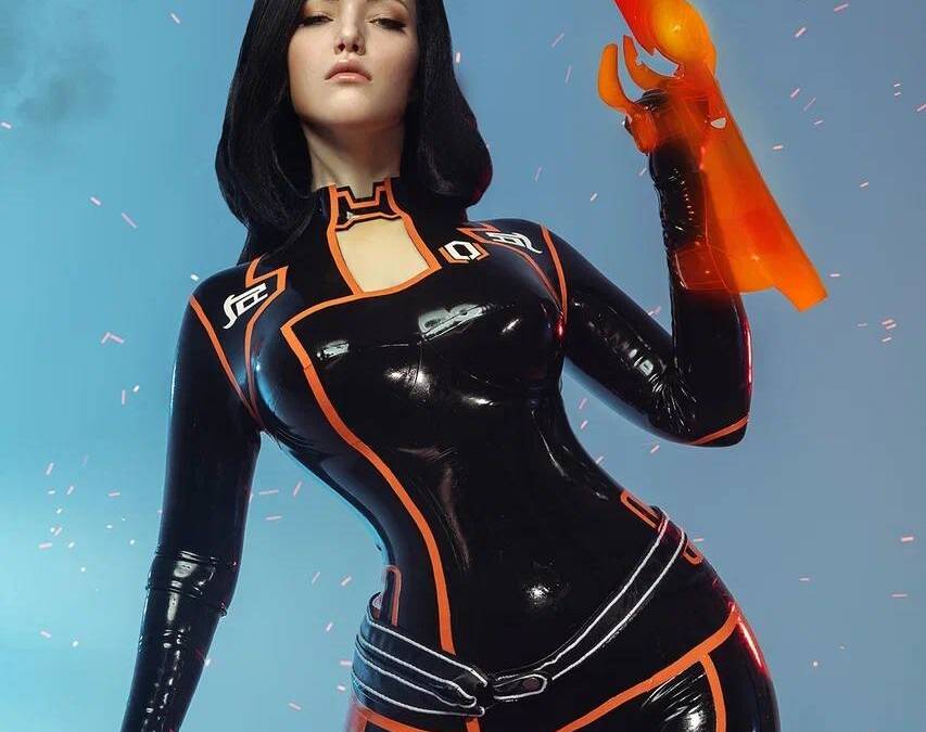 Косплей Миранды Лоусон из Mass Effect 2 от Лады Люмос в высоком каблуке стройная девушка в кожаном костюме с оранжевой отделкой с пистолетом в руке на фоне голубого неба