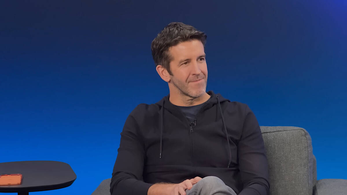 человек в чёрной куртке на кресле у синего фона Apple CEO Джон Тернус