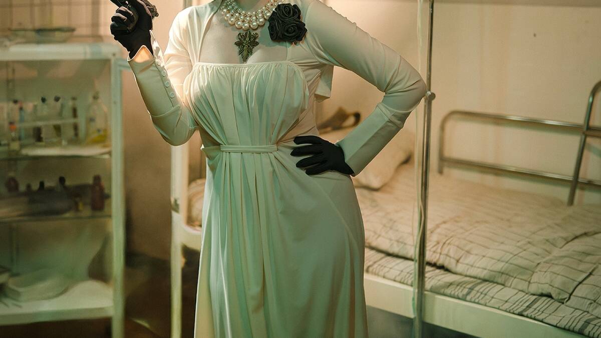 Косплей Грейс Эшкрофт из Resident Evil Requiem Dear Iris в костюме «Нуар» и «Димитреску» женщина в длинном платье шляпе и перчатках держит пистолет рядом с кроватью в больнице