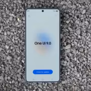 Смартфон Galaxy S26 с экраном загрузки One UI 9.0 на улице на гравии