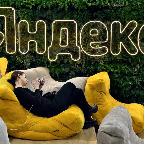 Женщина лежит на желтом диване в кафе с зеленой стеной и неоновым знаком Яндекс