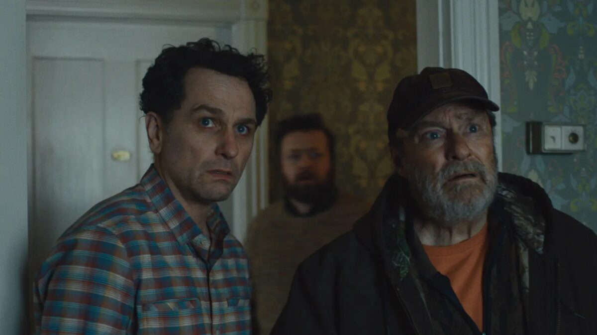 Два мужчины у двери, один в кепке, другой в клетчатой рубашке