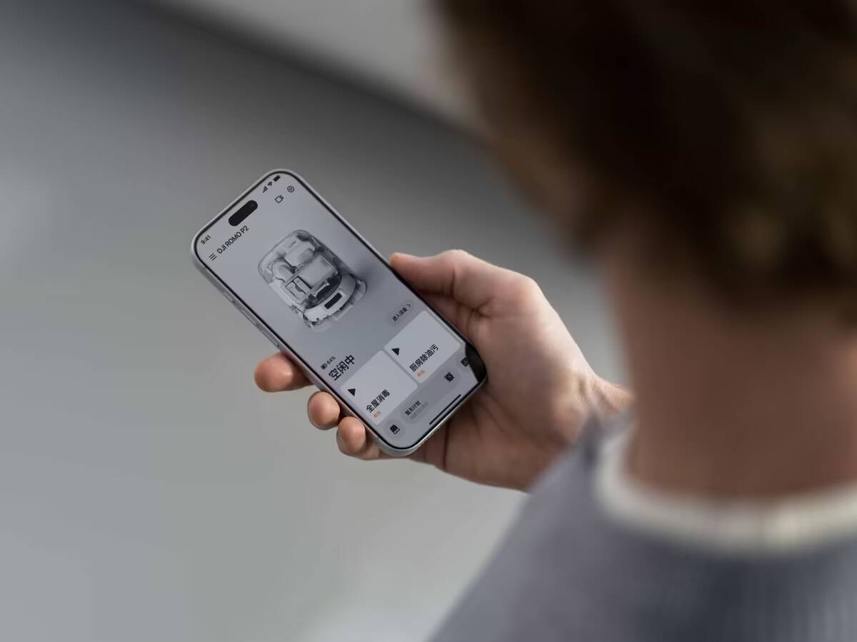 Человек с смартфоном управляет роботом-пылесосом DJI Romo 2