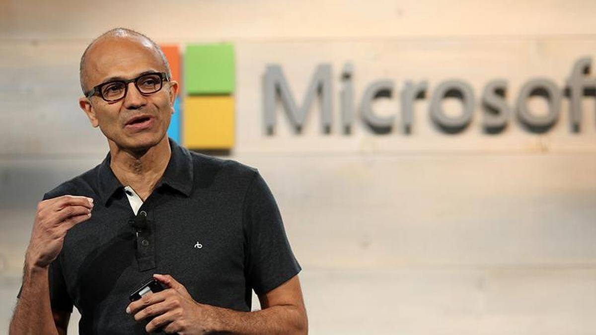 Мужчина с гнутым жестом и в черной рубашке у логотипа Microsoft