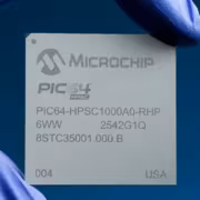 микросхема Microchip PIC64-HPSC1000A0-RHP в руке в голубых перчатках