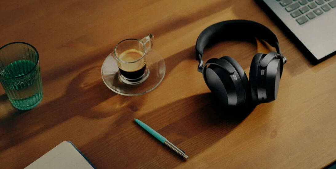 На столе лежат наушники Sennheiser Momentum 5 чашка с кофе чашка с водой ручка и ноутбук
