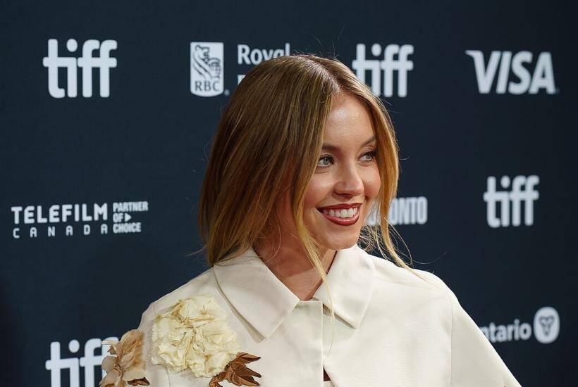 Сидни Суини улыбается на красной дорожке TIFF с белым платьем и цветочным декором